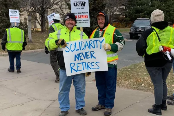 Photo of two retirees holding a sign that says "Solidarity Never Retires."
