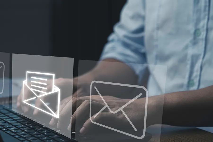 A person's hands typing on a keyboard with email icons super imposed in front of them.